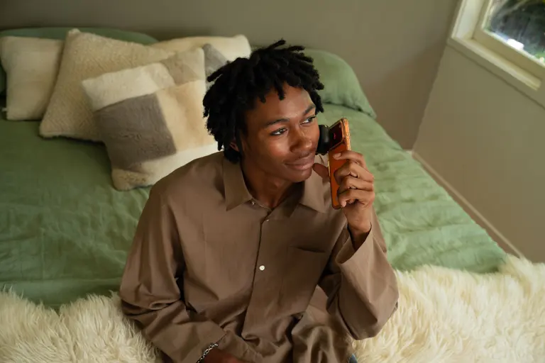 A man scanning his cheek with the Lumoscope while sitting on his bed in morning light.