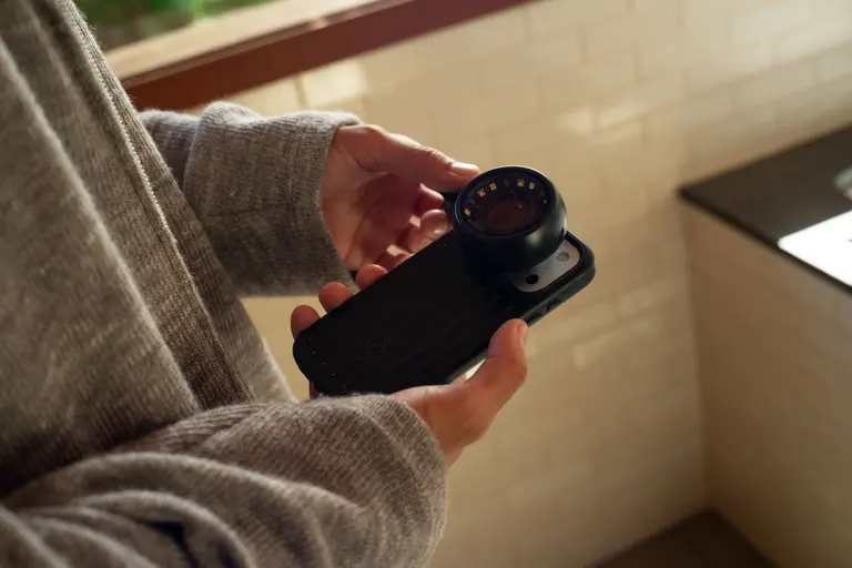 Hands clipping the Lumoscope onto a phone at a bathroom counter.