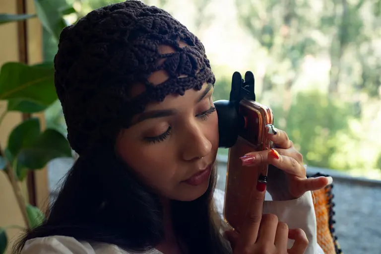 A woman holding the Lumoscope to her cheek by a bright window, mid-scan.