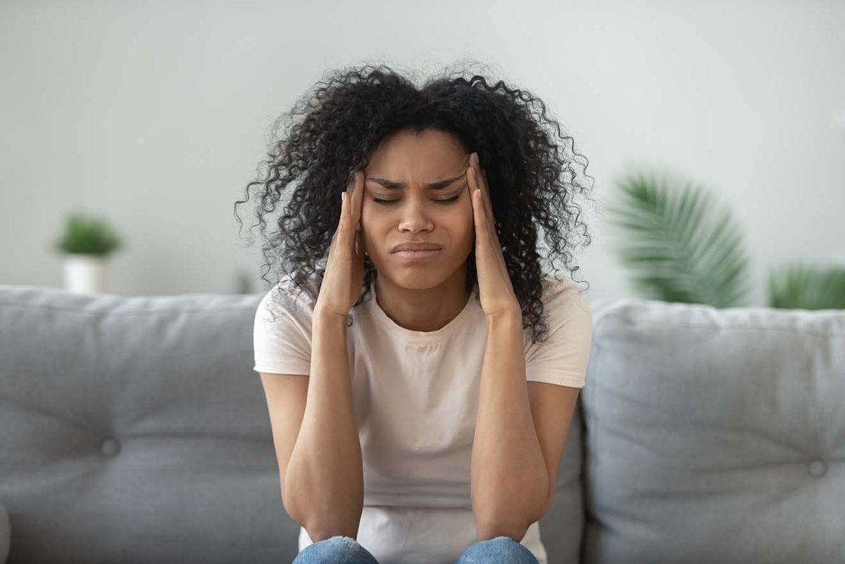 A woman sitting on a couch holding her head, looking distressed